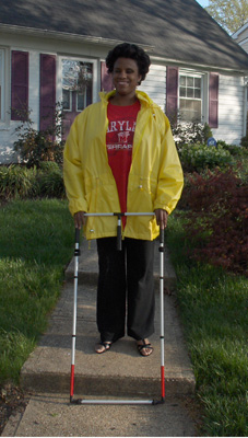 Photo shows Kelly smiling and standing on the sidewalk in front of her home.  The AMD has just dropped over the edge of a step.